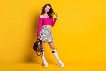 Fototapeta na wymiar Full length photo of lady curly hairdo look empty space hold bag play curl wear pink top unclothed shoulders mini skirt white stockings sneakers isolated yellow color background