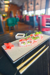 Salmon and caviar sushi rolls served on a traditional plate on a wooden table in a restaurant.