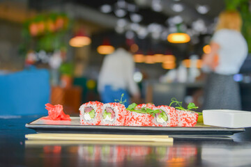 Salmon and caviar sushi rolls served on a traditional plate on a wooden table in a restaurant.