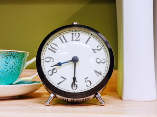 An alarm clock with a black body and silver legs stands on a wooden table