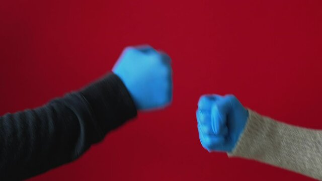 Alternative greeting. COVID-19 hygiene. Quarantine safety measures. New normal. Friends hands in blue protective gloves showing funny fist bump hi or bye gesture isolated on red background loop.