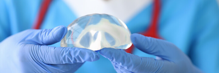 Gloved doctor holds female breast implant in his hands. Plastic surgery and mammoplasty concept