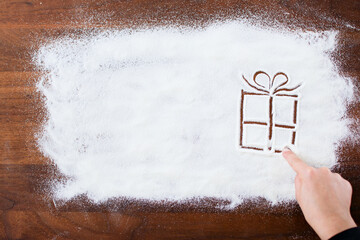 Christmas gift box sketch on flour background. Flour spread on the wooden table. White flour looks...