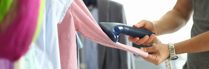 Man holds steamer in his hands and ironing shirt on hanger. Himchitska at home concept