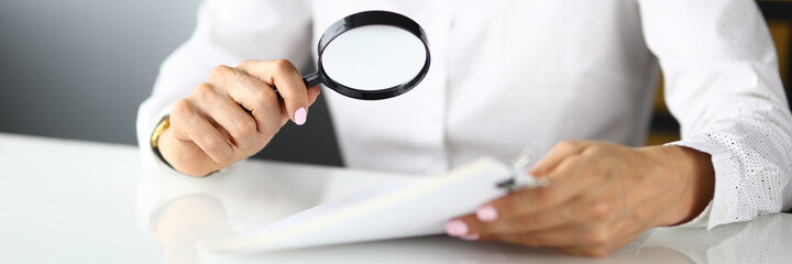 Woman sits at table and holds magnifying glass and documents in her hands. Search for new solutions in business concept