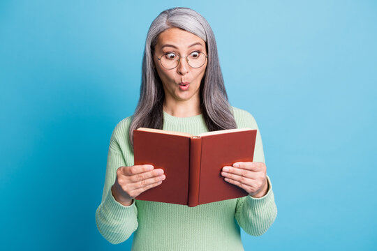 Photo portrait of shocked woman reading red book holding in two hands isolated on pastel light blue colored background