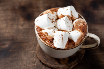 Hot cocoa or hot chocolate with marshmallows in a ceramic Cup on a brown wooden table