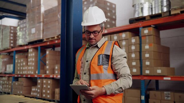 Caucasian male checking business males on digital tablet smiling standing along side packaged parcels in warehouse