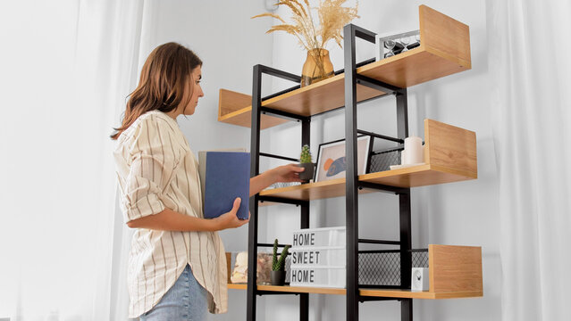 home improvement, decoration and people concept - woman arranging flower and books on shelving