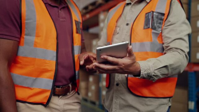 Close up of business men scrolling through deliveries on digital tablet standing in factory 