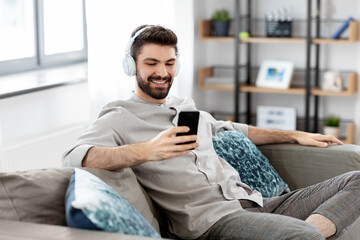 Obraz premium technology, leisure and people concept - happy man in headphones with smartphone listening to music at home