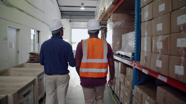 Manager and worker walking through isle double checking order of packaged parcels in factory warehouse 