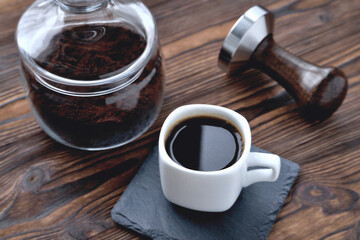 coffee in a cup on a stone stand, glass jar with coffee beans and coffee tamper, wooden natural background