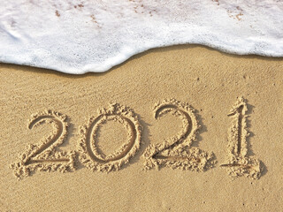 2021 text writing on the beach sand with wave are coming