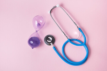 stethoscope and broken hourglass on pink background