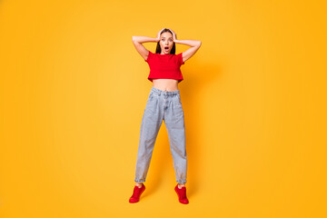 Full size photo of shocked lady hands on head stand on toes wear red crop top jeans shoes isolated on yellow color background