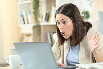Amazed woman checking good news on laptop at home