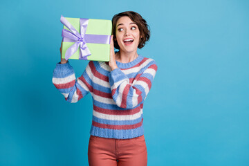 Photo portrait of funny short haired girl trying to guess what is in gift box isolated on vivid blue color background