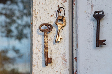 Old rusty key on the shabby wooden door frame with broken white paint and a blurred reflection of a nature on a dirty glass