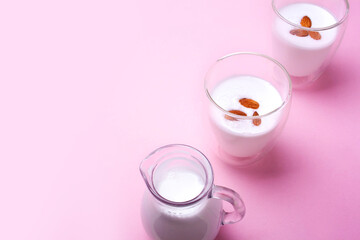 Almond milk in a decanter and two glasses on a pink background. Empty space for text