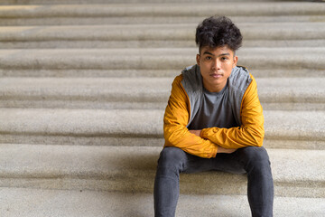 Obraz premium Young Asian man sitting with arms crossed on staircase in the city