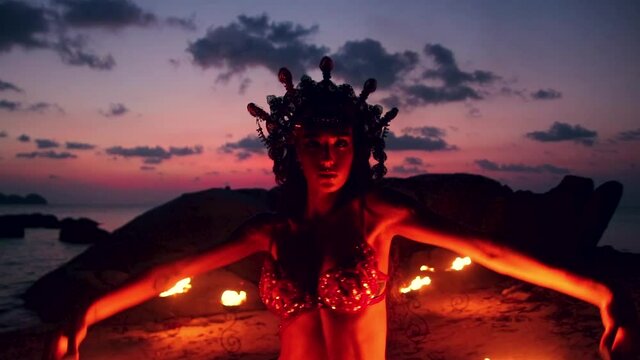 Erotic and sensual belly dancer, performing sexy moves with fire palm torch props, on the beach during golden hour. Close up.