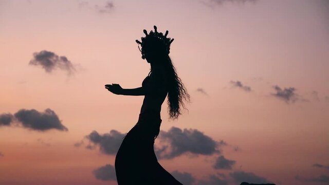 Close up of sexy, elegant and erotic arabian woman performing belly dance on the beach during golden hour. Silhouette.