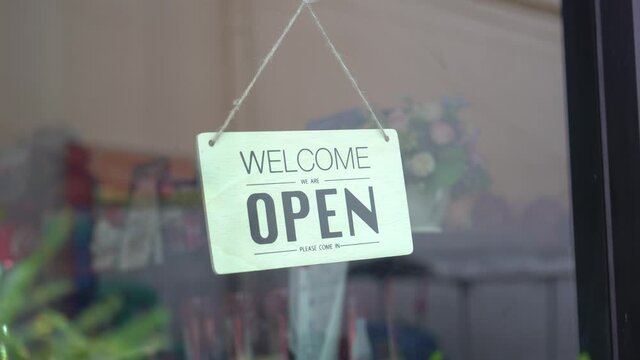 Asian woman wear mask turning Welcome we are open sign on fronton glass door cafe. Reopening activity after COVID-19, ended the lockdown and quarantine. Restarting again and keep forward concept.