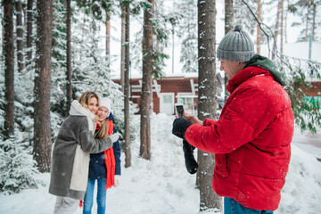 During a walk through the winter forest, a father takes photos of a mother and daughter on a smartphone.