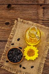 Sunflower oil in glass cruet with flower head and seeds in wooden bowl