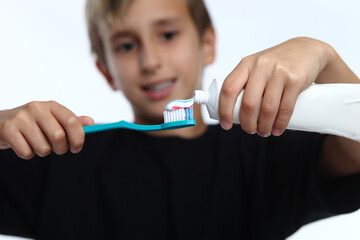 boy in white t-shirt squeezes toothpaste on brush and prepares to brush his teeth.