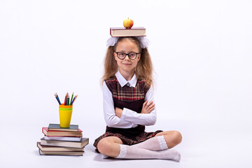 A little girl in a school uniform and glasses sits on a white background next to a pile of books.