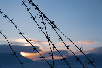 Old barbed wire against the background of the sunset sky and the winter landscape. Barbed wire closeup. Shallow depth of field. Siberia, Russia.
