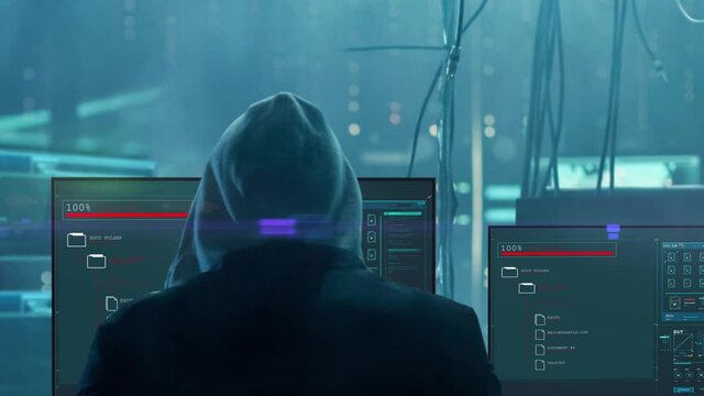 Hacker man sits with his back against the background of working computer screens.