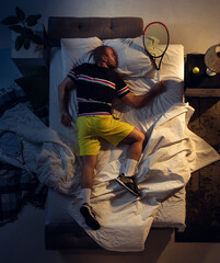 Passioned. Top view of young professional tennis player sleeping at his bedroom in sportwear with racket. Loving his sport even more than comfort, watching match even if resting. Action, motion, humor