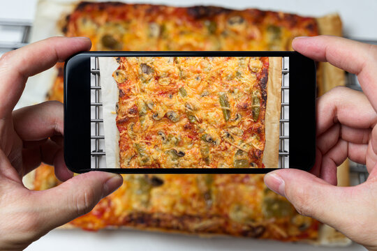 Man's hands taking a picture of a pizza with his cell phone