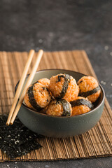 A bowl of rice balls with sesame seeds and nori seaweed, served with soy sauce, chopsticks