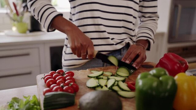 Midsection of woman standing by kitchen table cutting fresh zucchini with knife for salad