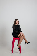 Girl in black studio dresses sits on red chair