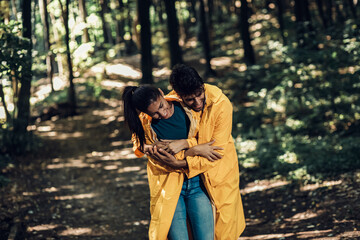 Young couple enjoys walking through the woods in raincoats after the rain.