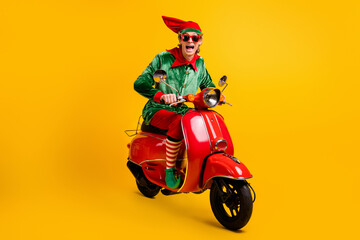 Portrait of his he nice attractive cheerful cheery glad ecstatic funny guy elf riding red moped having fun festal look sale discount isolated over bright vivid shine vibrant yellow color background