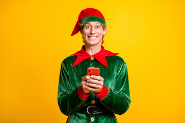 Portrait of his he nice attractive glad cheerful cheery funny guy elf using device app 5g blogging post smm like follow isolated over bright vivid shine vibrant yellow color background