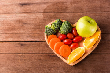 Top view of fresh organic fruits and vegetables in heart plate wood (apple, carrot, tomato, orange, broccoli) on wooden table, Healthy lifestyle diet food concept.