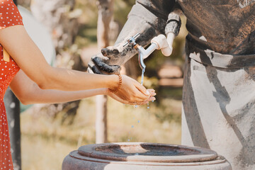Happy woman washes her hands on the street in a spring fountain in the form of a sculpture of a water carrier.