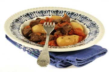 Morceaux de viande de boeuf mijotés avec des carottes et des pommes de terre servis dans une assiette en gros plan sur fond blanc