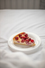 Piece of classic New York cheesecake with raspberry berries on a white plate on the bed. Close up view