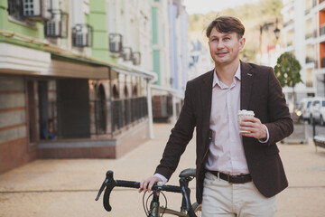 Attractive stylish man enjoying coffee walking in the city with his bike