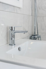 Faucet with a drop of water and a sink on a background of gray tiles. Bathroom interior after renovation. Saving water concept.