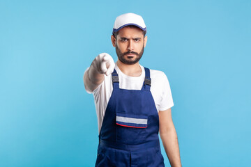 Hey you! Portrait of strict handyman in overalls and cap pointing finger to camera. Profession of service industry, post and delivery, engineer builder job. Expert repairman in workwear making choice