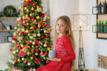 beautiful girl near the christmas tree. child sits with a cup of tea at christmas time.